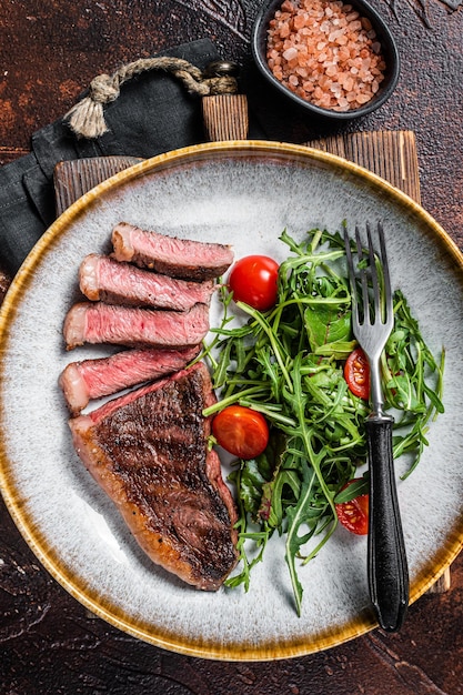 Bistecca di manzo con controfiletto alla griglia in piastra con insalata di verdure Sfondo scuro Vista dall'alto