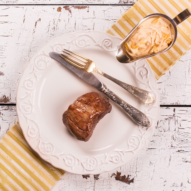 Bistecca di manzo con salsa di cipolla sul tavolo in legno bianco.