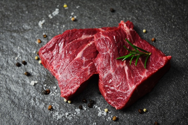 Bistecca di manzo cruda con erbe e spezie. Manzo della carne fresca affettato sul nero