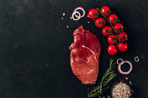 Bistecca di manzo cruda con sale e pepe al rosmarino su sfondo di pietra nera Vista dall'alto