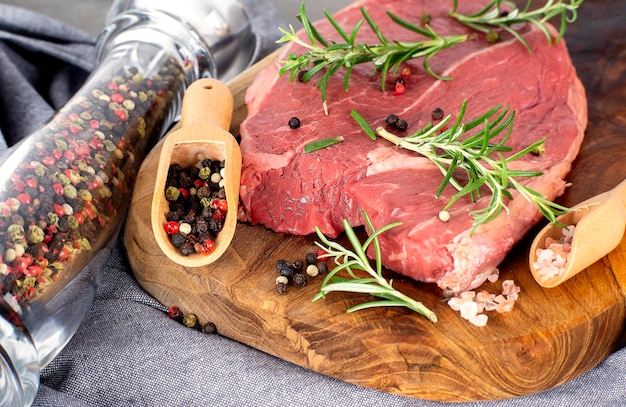 Bistecca di manzo di carne cruda con cucchiaio di legno pepe e macina sale e pepe sul tagliere di legno su un grembiule grigio