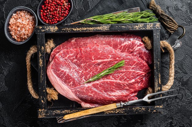 Bistecca di manzo marmorizzata carne cruda con spezie in vassoio di legno Sfondo nero Vista dall'alto