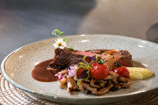 Bistecca di manzo mediamente rara e funghi affettati fritti sono decorati da un piccolo fiore su un piatto bianco pronto da servire e mangiare