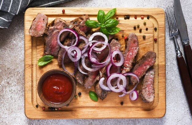 Bistecca di manzo rara con cipolla, fetta su una tavola di legno. Vista dall'alto.