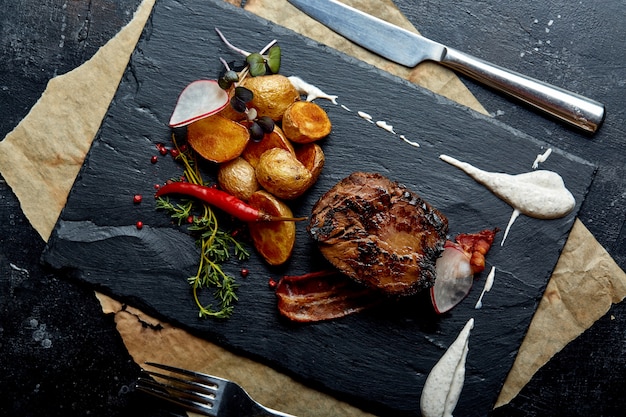 Bistecca di manzo servita con patate e verdure al forno, superficie nera, primo piano. cibo di concetto.