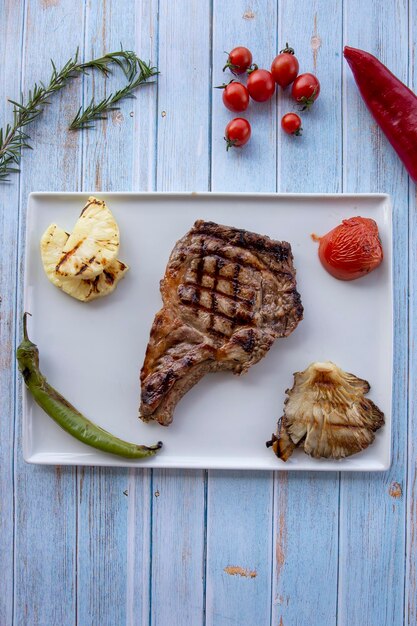 Bistecca di manzo su fondo di legno blu con pomodori arrostiti, cipolle e peperoni