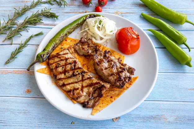 Bistecca di manzo su fondo di legno blu con pomodori arrostiti, cipolle e peperoni