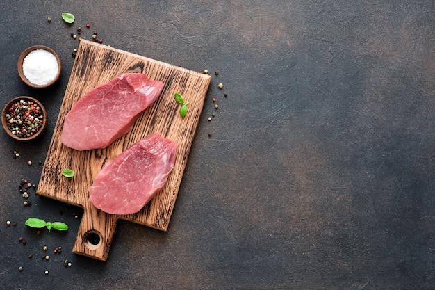 Bistecca di manzo su una tavola di legno con spezie su uno sfondo concreto.