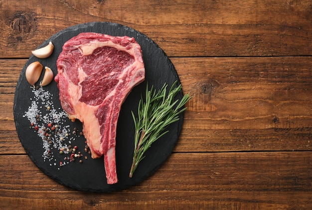 Bistecca di manzo tomahawk cruda con ingredienti per grigliare rosmarino sale pepe e aglio