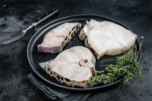 Bistecca di pesce lupo o wolffish crudo fresco su un piatto. Tavolo nero. Vista dall'alto.