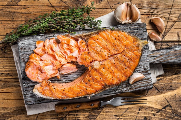 Bistecca di pesce trota salmone alla griglia su una tavola di legno con erbe aromatiche. Fondo in legno. Vista dall'alto.