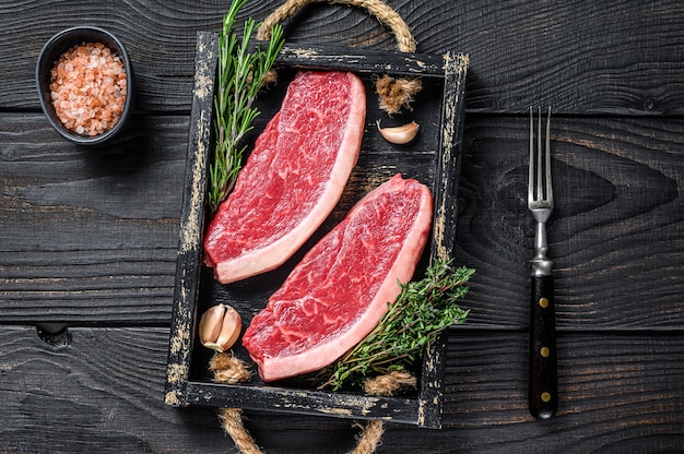 Bistecca di picanha brasiliana cruda o bistecca di carne di manzo controfiletto superiore in un vassoio di legno. Fondo in legno nero. Vista dall'alto.