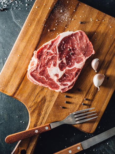 bistecca di ribeye con tavola da taglio in legno su sfondo nero di pietra