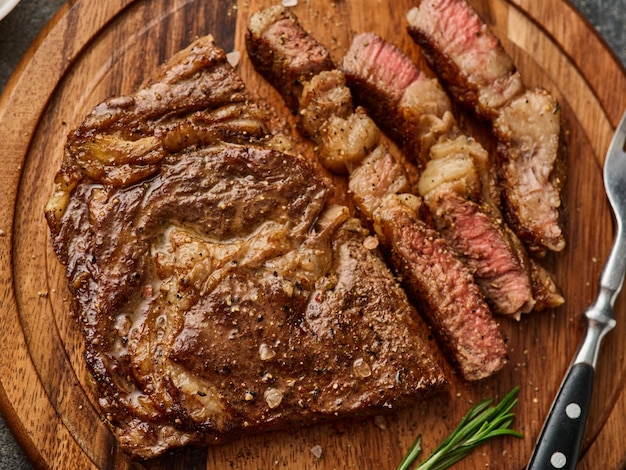 Bistecca di Ribeye o bistecca di manzo mediamente rara sul vassoio di legno con erbe Vista dall'alto da vicino