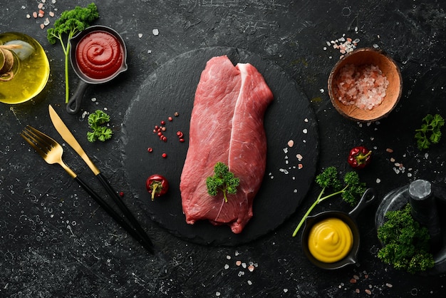 Bistecca di vitello bistecca di manzo filetto di carne cruda biologica su sfondo di pietra di ardesia nera Vista dall'alto Carne cruda