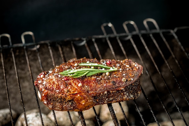 Bistecca piccante alla griglia su un barbecue estivo sui carboni ardenti guarnita decorata con un ramo di rosmarino. Cucinare il cibo. avvicinamento