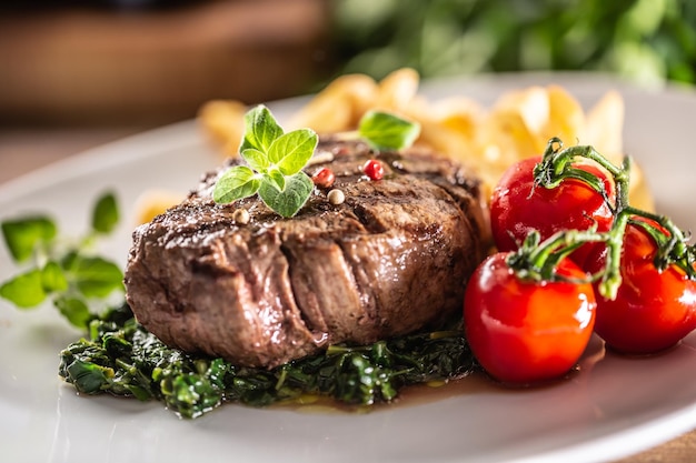 Bistecca spessa alla griglia con pomodorini, spinaci cotti e patatine fritte