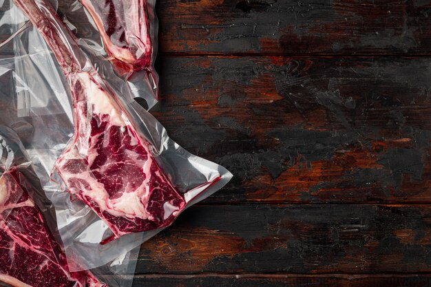 Bistecca stagionata a secco sottovuoto. Prodotti a base di carne in confezione di plastica, tomahawk, t bone e tagli di bistecca club, su vecchio tavolo di legno scuro, vista dall'alto piatta