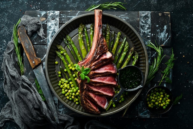 Bistecca Tomahawk con osso Bistecca alla griglia con asparagi e piselli su sfondo nero Vista dall'alto Spazio di copia gratuito