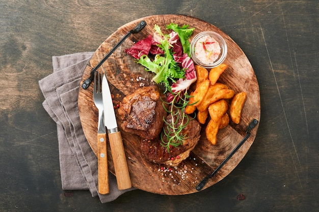 Bistecche Bistecca di carne alla griglia a fette New York Ribeye o Chuck roll con guarnito con insalata e patatine fritte su tavola di marmo nero su sfondo di legno vecchio Vista dall'alto Mock up