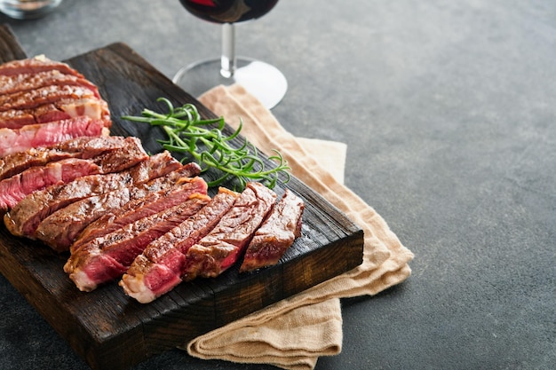 Bistecche Bistecca di carne alla griglia affettata New York o Ribeye con spezie rosmarino e pepe su tavola di marmo nero su sfondo di legno vecchio Vista dall'alto Mock up