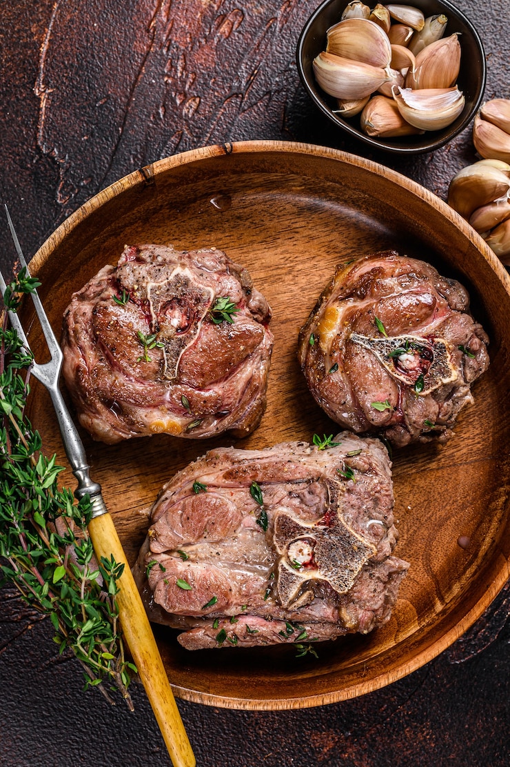 Foto bistecche di carne di collo di agnello fritte in un piatto di legno con erbe aromatiche. sfondo scuro. vista dall'alto.