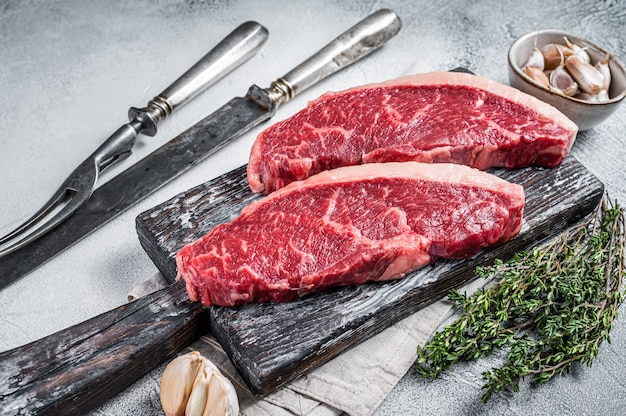 Bistecche di carne di manzo crudo su tavola di legno con coltello da carne e forchetta. Sfondo bianco. Vista dall'alto.