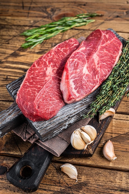 Bistecche di carne di manzo della lama superiore della spalla cruda su un bordo di legno del macellaio con le erbe. fondo in legno. Vista dall'alto.