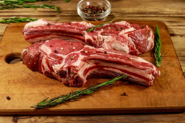 bistecche di carne fresca cruda su ossa con spezie e rosmarino su tavola di legno