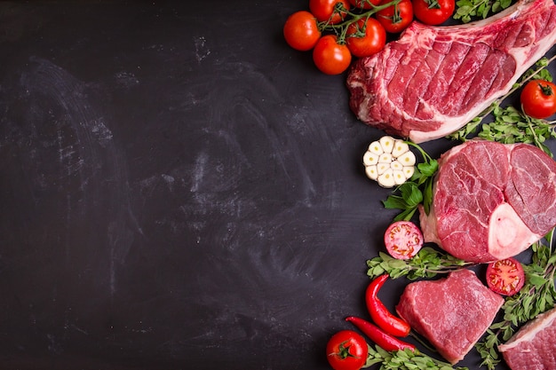 Bistecche di carne succosa cruda pronte per la tostatura su uno sfondo di lavagna nera.