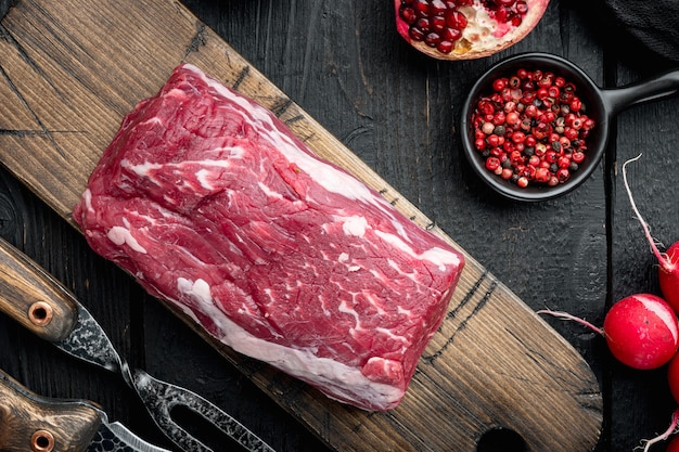 Bistecche di filetto di manzo crudo con spezie e intero filetto marmorizzato tagliato insieme, sul tavolo di legno nero, vista dall'alto laici piatta