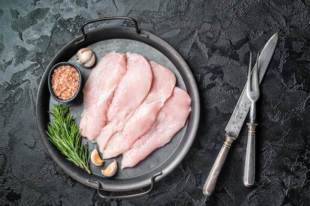 Bistecche di filetto di petto di pollo a fette crude in un vassoio d'acciaio Carne di pollo Sfondo nero Vista dall'alto