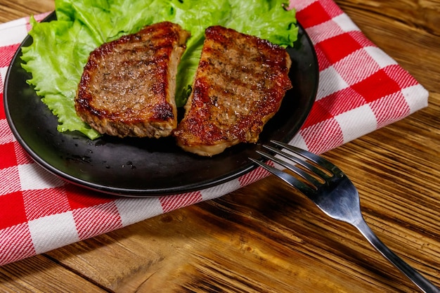 Bistecche di maiale alla griglia con foglie di lattuga sulla tavola di legno