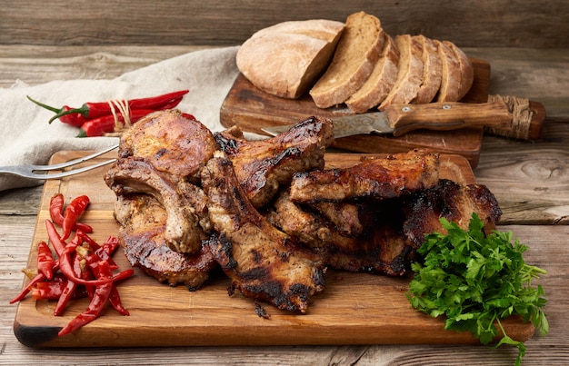 Bistecche di maiale alla griglia con osso su un tagliere da cucina, pane di farina di segale affettato al forno e peperoncino rosso