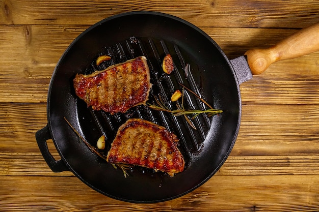 Bistecche di maiale alla griglia con rosmarino, aglio e spezie in padella in ghisa su tavola di legno Vista dall'alto