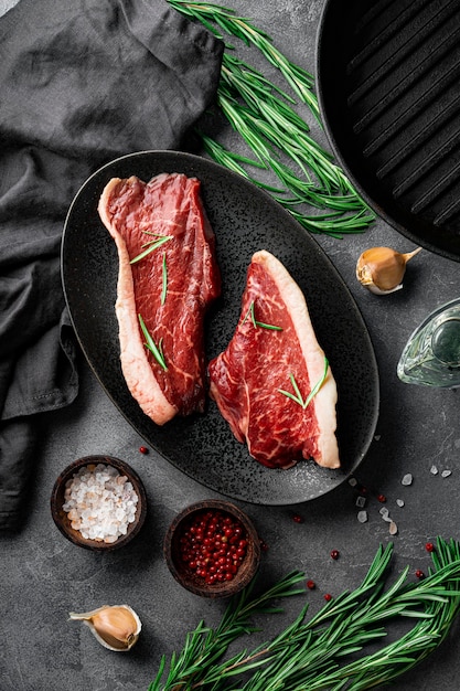 Bistecche di manzo marmorizzate crude e condimenti per la loro preparazione, vista dall'alto. Carne di manzo cruda sulla foto verticale del tavolo da cucina. Foto di alta qualità