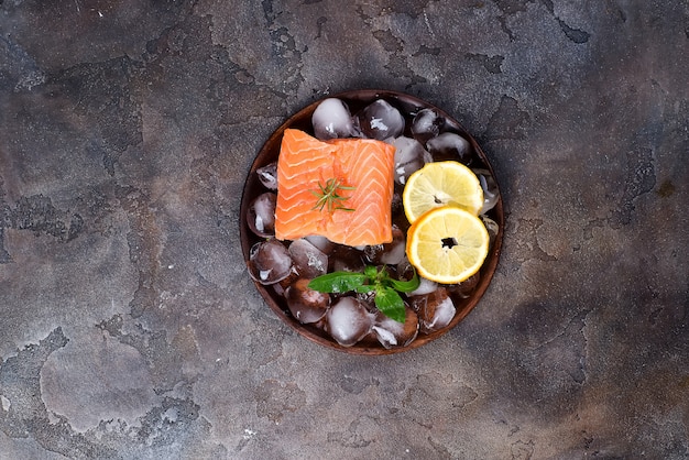 Bistecche di salmone su ghiaccio con fetta di limone sul piatto di legno. Proteine ​​magre.