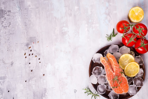 Bistecche di salmone su ghiaccio con fettina di limone sul piatto di legno con pomodoro