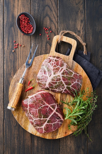 Bistecche Raw Raw bistecca da cowboy carne di manzo marmorizzata con spezie rosmarino e pepe su tavola di legno nera su vecchio sfondo di tavolo in legno scuro Vista dall'alto Mock up