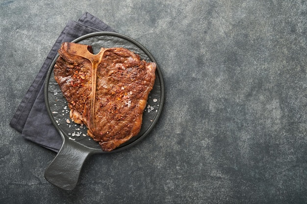 Bistecche Tbone Fette di manzo alla griglia Tbone o bistecca di carne porterhouse con spezie rosmarino e pepe su tavola di marmo nero su fondo in legno vecchio Vista dall'alto Mock up