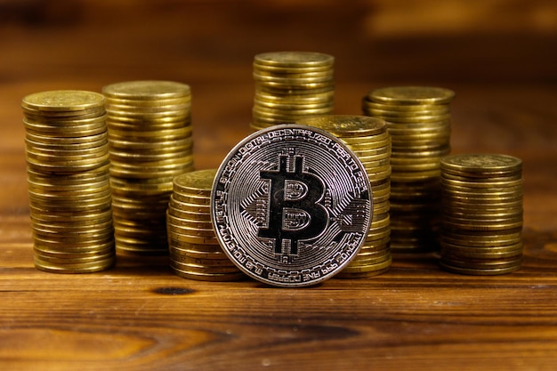 Bitcoin d'argento e pile di monete su fondo di legno