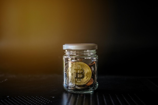 Bitcoin d'oro e moneta di denaro in un barattolo di vetro su sfondo nero Valuta Crypto e concetto di finanza