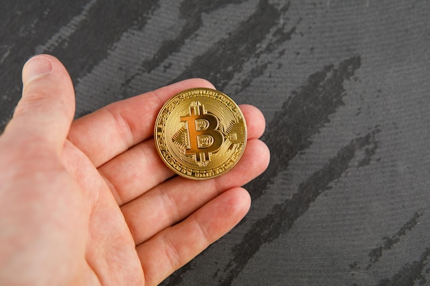 Bitcoin d'oro nelle mani dell'uomo sullo sfondo di un tavolo di legno