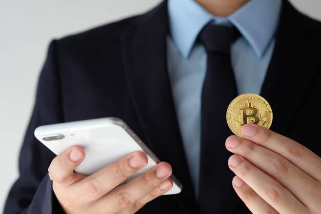 Bitcoin della tenuta della mano dell&#39;uomo d&#39;affari e smartphone usando sopra fondo bianco