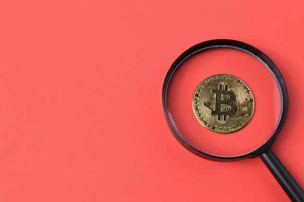 Bitcoin e lente di ingrandimento su sfondo rosso con spazio di copia