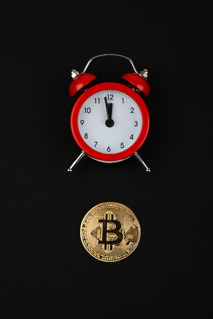 Bitcoin e sveglia rossa su fondo nero. Concetto di criptovaluta. Moneta color oro.