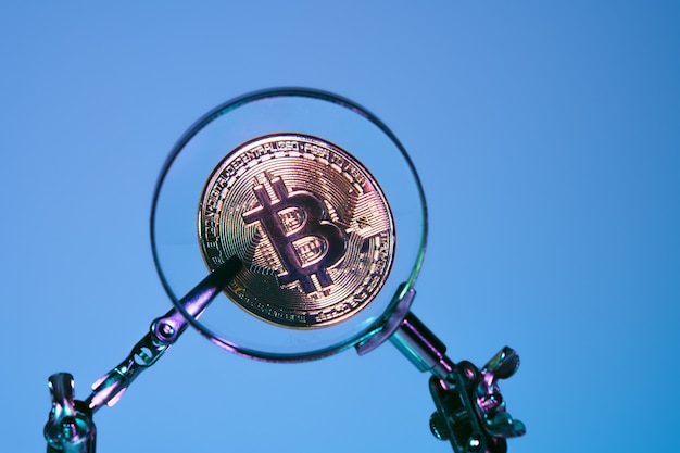 Bitcoin oro isolato visto con una lente di ingrandimento su sfondo blu. criptovaluta e denaro