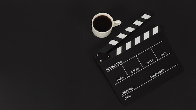 Black Clapper board e tazza bianca di caffè caldo su sfondo nero.