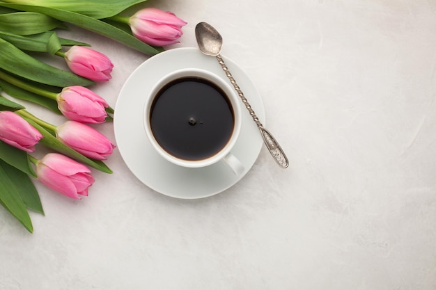 Black coffee in white Cup with pink tulips on light stone background Top view with copy space