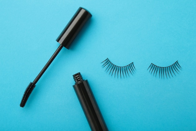 Black eyelashes and mascara on blue background. Top view. Beauty concept